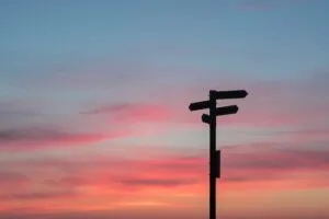 Image of a silhouette of direction signs against a sun-setting sky to illustrate post