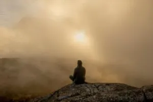 Image of person sat on a mountain in the mist, with the sun trying to break through to illustrate post