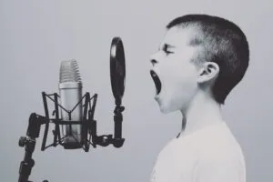 Image of child shouting or screaming into a microphone with spitguard in front to illustrate post