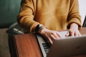 Image of person wearing yellow jumper and bangles on right wrist, typing on laptop keyboard, to illustrate post