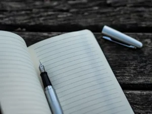 Image of a fountain pen lying on a lined notebook, with the cap removed, lying on the side, used to illustrate post