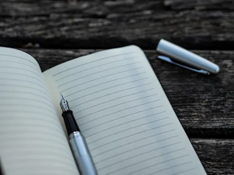 Image of a fountain pen lying on a lined notebook, with the cap removed, lying on the side, used to illustrate post